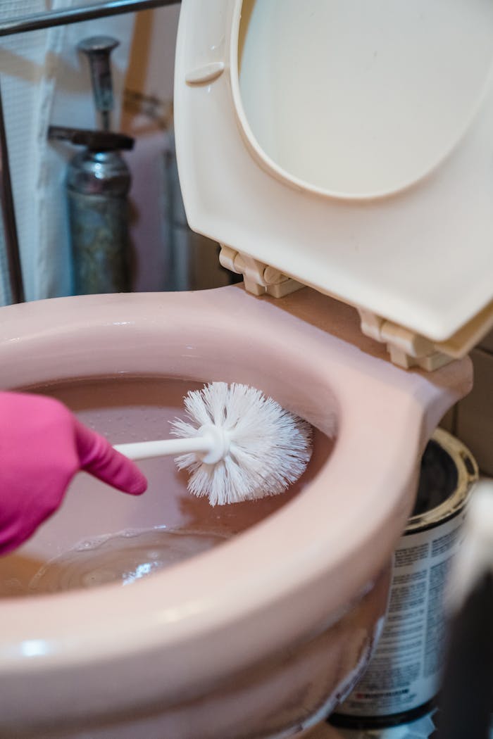 A detailed view of cleaning a toilet bowl with a brush and gloves.